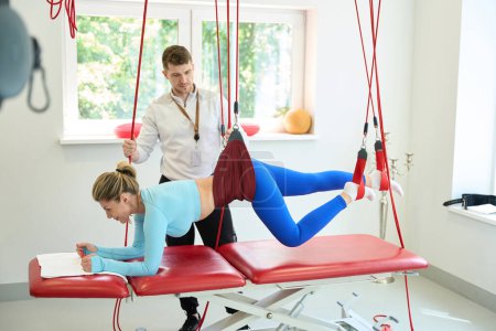 Foto de Hermosa mujer haciendo terapia de suspensión con entrenador mediante el uso de la cuerda roja en la clínica de fitness - Imagen libre de derechos