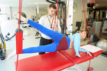 Foto de Mujer atractiva haciendo terapia de suspensión con entrenador mediante el uso de cordón rojo en el gimnasio - Imagen libre de derechos