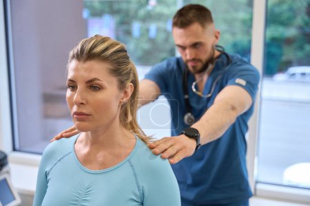 Téléchargez les photos : Orthopédiste qualifiée examinant la patiente, regardant la position de ses épaules et de sa colonne vertébrale, évaluant le bien-être et l'état général du corps, pratiquant l'ostéopathie - en image libre de droit