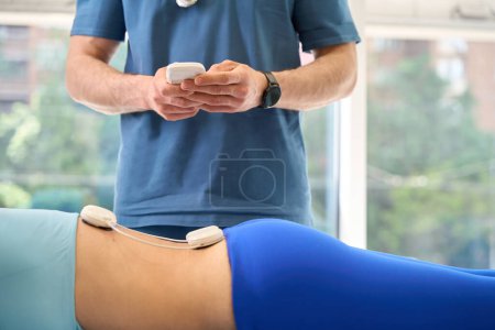 Foto de Traumatólogo masculino programando la fuerza de los sensores magnit para involucrar a todos los grupos musculares de la paciente femenina en el proceso de curación, trauma de la columna vertebral - Imagen libre de derechos