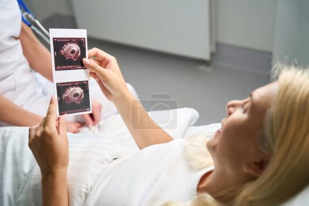 Foto de Mujer feliz paciente sostiene imágenes de ultrasonido en sus manos, se comunica con el médico en la habitación del hospital - Imagen libre de derechos
