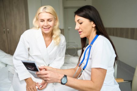 Foto de Dos hermosas mujeres se encuentran en una habitación de hospital, el médico y el paciente están mirando imágenes de ultrasonido - Imagen libre de derechos
