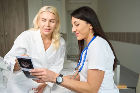 Foto de Dos damas están sentadas en una habitación de hospital, un médico y un paciente están mirando imágenes de ultrasonido - Imagen libre de derechos