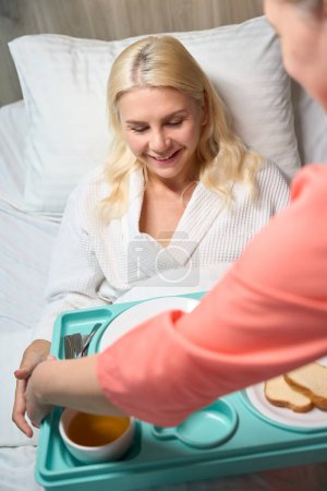 Foto de Empleado del centro médico está cuidando a una mujer en reposo en cama, ella trajo su comida dietética - Imagen libre de derechos
