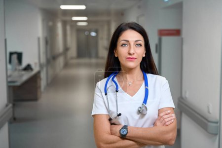Téléchargez les photos : Médecine dans un couloir lumineux de l'hôpital, elle a un stéthoscope sur le cou - en image libre de droit