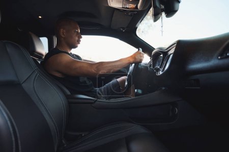 Téléchargez les photos : Beau Afro-Américain conduisant pour travailler dans son automobile de luxe avec ordinateur de bord et climatisation - en image libre de droit