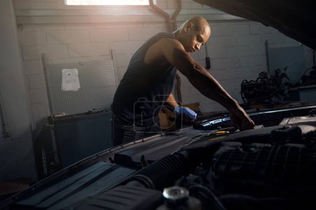 Photo for Concentrated African American man checking level of oil and glass washer, spending time in his garage repairing car, male hobby, motor vehicle service station - Royalty Free Image
