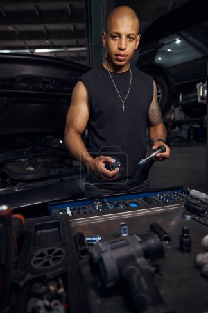 Photo for Qualified automotive mechanic taking proper sockets and adjusting screwdrivers repairing car in his motor vehicle service station, adjustment and alteration of some component of motor vehicle - Royalty Free Image