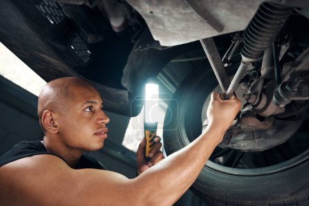 Photo for African American auto mechanic checking condition of car running system after accident, lighting with additional lamp to see a crack or bent on spare part, automobile repair shop - Royalty Free Image