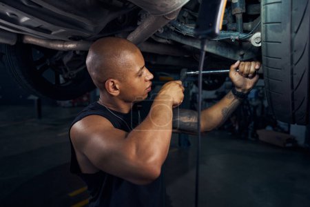 Photo for Serious African American repairman checking the condition and reliability of fastening of front suspension arms to the ball joint, repairing car in motor vehicle service station - Royalty Free Image
