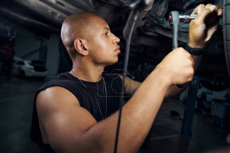 Photo for Handsome concentrated African American auto-mechanic holding open-end wrench, unscrewing ball joint arms, engaging in car components reconditioning and alteration - Royalty Free Image