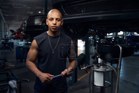Photo for African American bulking auto-mechanic holding many wrenches in hands and looking at camera, owning garage where engaging in car tuning and pimp, business - Royalty Free Image