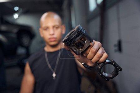 Photo for Self-confident automotive mechanic holding and showing to camera piston with crank mechanism, adjusting engine and changing piston system rings, motor vehicle service station - Royalty Free Image