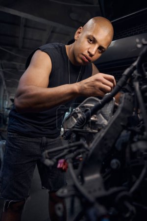 Téléchargez les photos : Réparateur afro-américain chauve travaillant avec moteur de voiture, nettoyage des pièces et vérification du niveau d'usure, mécanisme de réglage, station-service pour véhicules automobiles - en image libre de droit