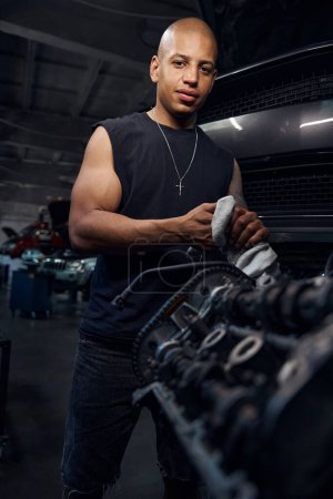 Photo for Happy smiling African American man auto-mechanic cleaning hands after successful engine repairing, enjoying his qualitative work in motor vehicle service station - Royalty Free Image