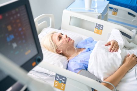 Téléchargez les photos : Femme après la chirurgie se trouve dans une pièce avec un équipement moderne pour surveiller les fonctions vitales des patients - en image libre de droit