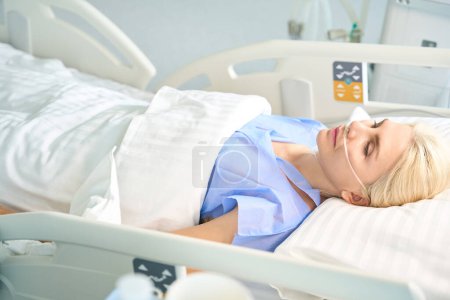Téléchargez les photos : Femme blonde après la chirurgie se trouve dans une pièce avec un équipement moderne pour surveiller les fonctions vitales des patients - en image libre de droit