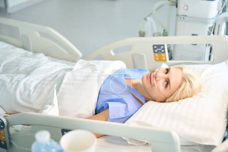 Téléchargez les photos : Belle femme après la chirurgie se trouve dans une pièce avec un équipement moderne pour surveiller les fonctions vitales des patients - en image libre de droit