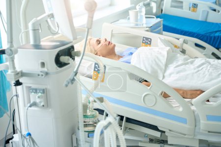 Lady lies on a special bed, she is connected to medical equipment to monitor the patients vital activity
