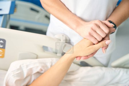 Foto de La enfermera sostiene a los pacientes de la mano, alienta a la dama después de la cirugía - Imagen libre de derechos