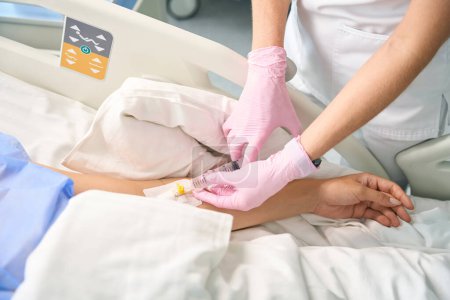 Foto de El trabajador sanitario realiza una inyección en una vena de un paciente con una jeringa grande, el personal médico usa guantes protectores - Imagen libre de derechos