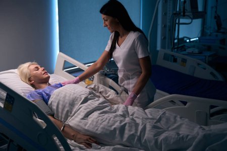 Téléchargez les photos : Médecin féminin en ronde dans la salle de réveil, le patient est connecté à une machine à oxygène - en image libre de droit