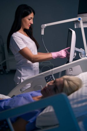 Foto de La doctora bonita usa equipo moderno en la sala de recuperación, el paciente se acuesta en una cama especial - Imagen libre de derechos