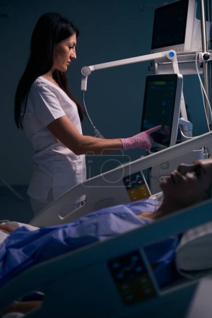 Foto de Médico femenino utiliza equipos modernos en la sala de recuperación, la paciente se encuentra en una cama especial - Imagen libre de derechos