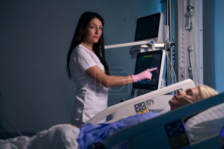Foto de Trabajadora médica utiliza equipos modernos en la sala de recuperación, la paciente se acuesta en una cama especial - Imagen libre de derechos