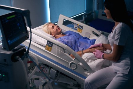 Téléchargez les photos : Une femme en uniforme médical communique avec un patient après une intervention chirurgicale dans un service hospitalier - en image libre de droit