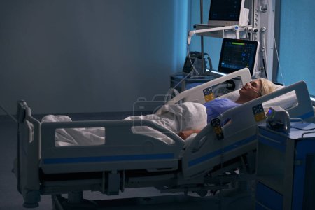 Foto de La mujer descansa después de la cirugía en la unidad de cuidados intensivos, está conectada a dispositivos médicos - Imagen libre de derechos