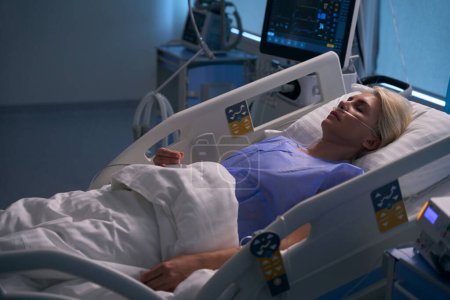Téléchargez les photos : Femme qui dort est dans l'unité de soins intensifs, elle est connectée à des dispositifs médicaux - en image libre de droit