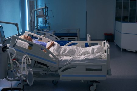 Téléchargez les photos : Femme en convalescence se trouve sur un lit postopératoire dans l'unité de soins intensifs, elle est connectée à des dispositifs médicaux - en image libre de droit