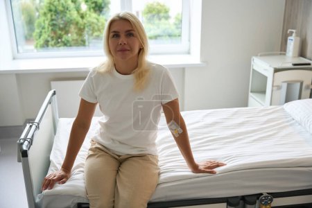 Foto de El paciente se sienta en una cama de hospital en una habitación luminosa, hay un desinfectante en la mesita de noche - Imagen libre de derechos
