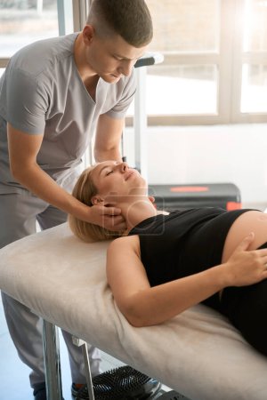 Photo for Massage therapist conducts a manual therapy session for a pregnant client, a specialist works with a womans neck - Royalty Free Image