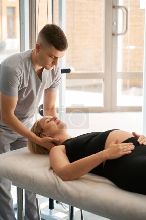 Photo for Young massage therapist conducts a manual therapy session for a pregnant woman, a specialist works with the clients neck - Royalty Free Image