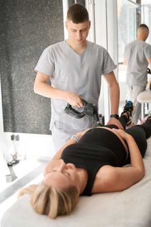 Photo for Young physiotherapist performs myostimulation on an expectant mother, using a special physiotherapeutic device - Royalty Free Image
