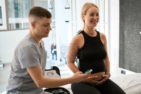 Photo for Physiotherapist in a wellness center uses hardware therapy, a pregnant client enjoys the procedure - Royalty Free Image