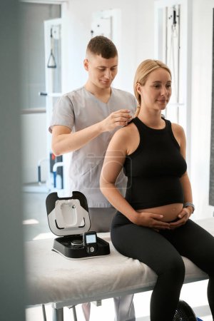 Photo for Physiotherapist conducts a hardware therapy session in a wellness center, a pregnant client enjoys the procedure - Royalty Free Image