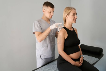 Reflexologe führt eine Akupunktursitzung an einer schwangeren Frau durch, der Spezialist arbeitet mit Schutzhandschuhen