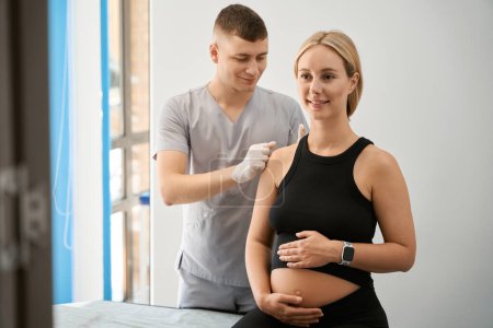 Téléchargez les photos : Réflexologue mène une séance d'acupuncture dans un centre de bien-être, la femme enceinte s'assoit sur une table de massage - en image libre de droit