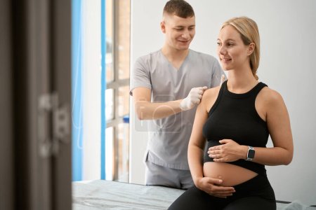 Téléchargez les photos : Spécialiste mène une séance d'acupuncture dans un centre de bien-être, une femme enceinte s'assoit sur une table de massage - en image libre de droit