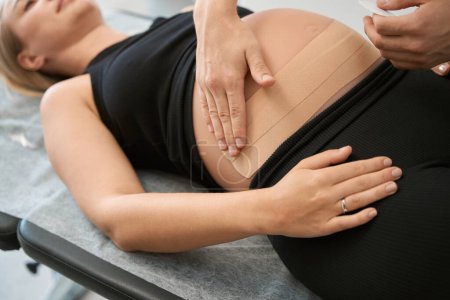 Foto de Terapeuta de rehabilitación golpea el vientre de una mujer embarazada, el cliente se acuesta en la mesa de masaje - Imagen libre de derechos