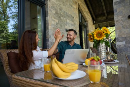 Photo for Happy couple high-fiving each other at the table, there are fruits and sunflowers on the table - Royalty Free Image
