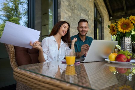 Photo for Man and a woman are working with documents on the terrace, there are fruits and sunflowers on the table - Royalty Free Image