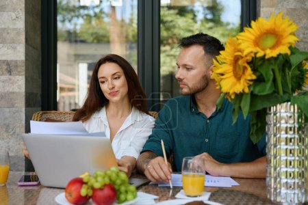Photo for Spouses work with documents on the terrace, there are fruits and sunflowers on the table - Royalty Free Image