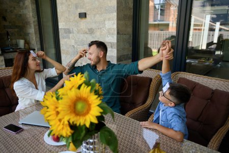 Foto de Los padres felices juegan con su hijo en la mesa durante un descanso entre el trabajo, la familia se encuentra en la terraza - Imagen libre de derechos