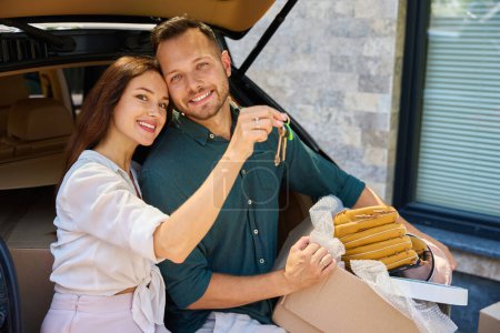 Téléchargez les photos : Couple, s'embrassant, sont assis dans le coffre ouvert d'une voiture, la femme a les clés dans ses mains. - en image libre de droit