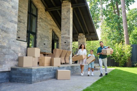 Photo for Parents and son move boxes with things to a new house, they chat cheerfully - Royalty Free Image