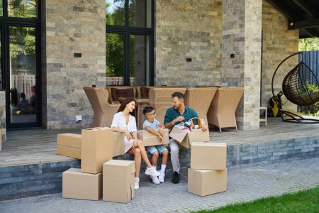 Photo for Family is resting on the terrace of a new house, they have a lot of cardboard boxes with things - Royalty Free Image